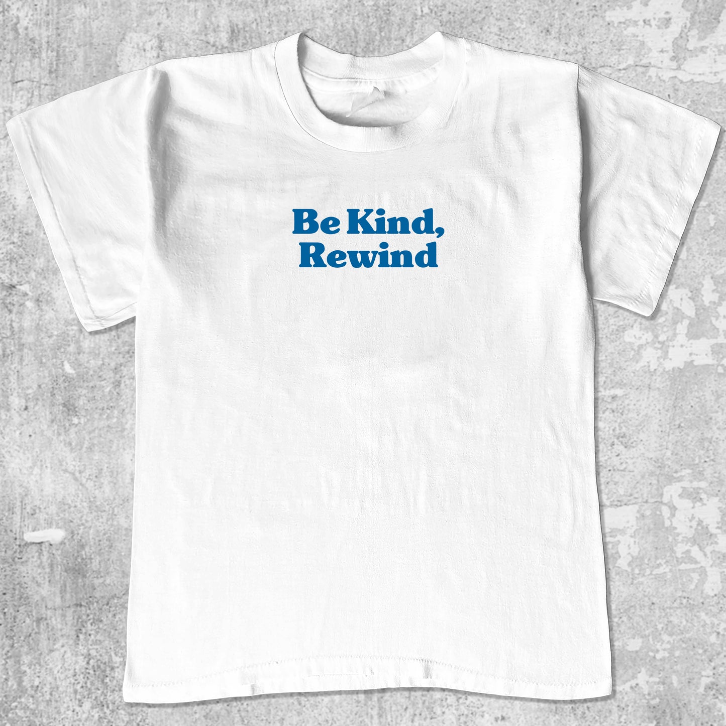 White t-shirt with be kind, rewind text on a gray textured background