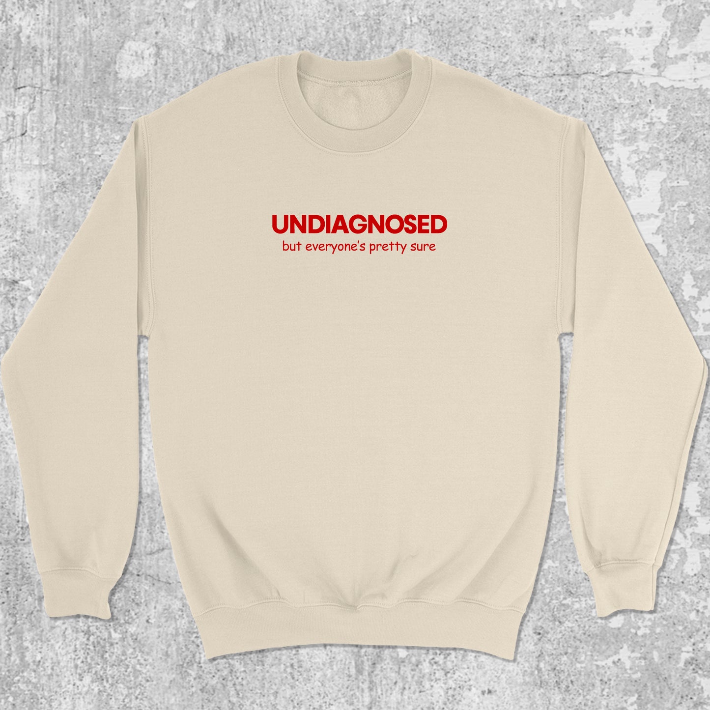 Beige sweatshirt with red text 'UNDIAGNOSSED but everyone's pretty sure' on a textured gray background