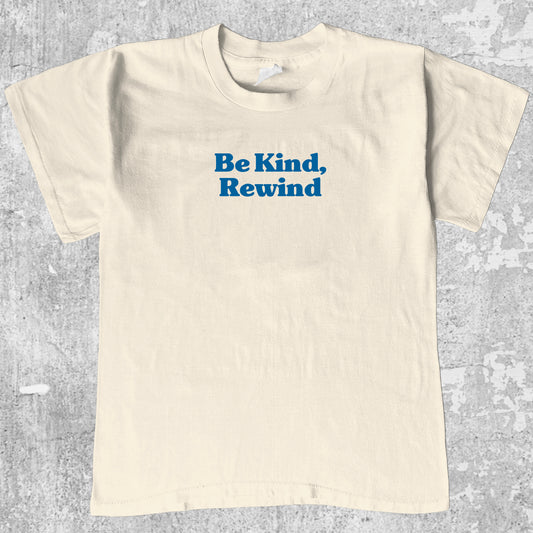 Beige t-shirt with 'Be Kind, Rewind' text on a gray textured background