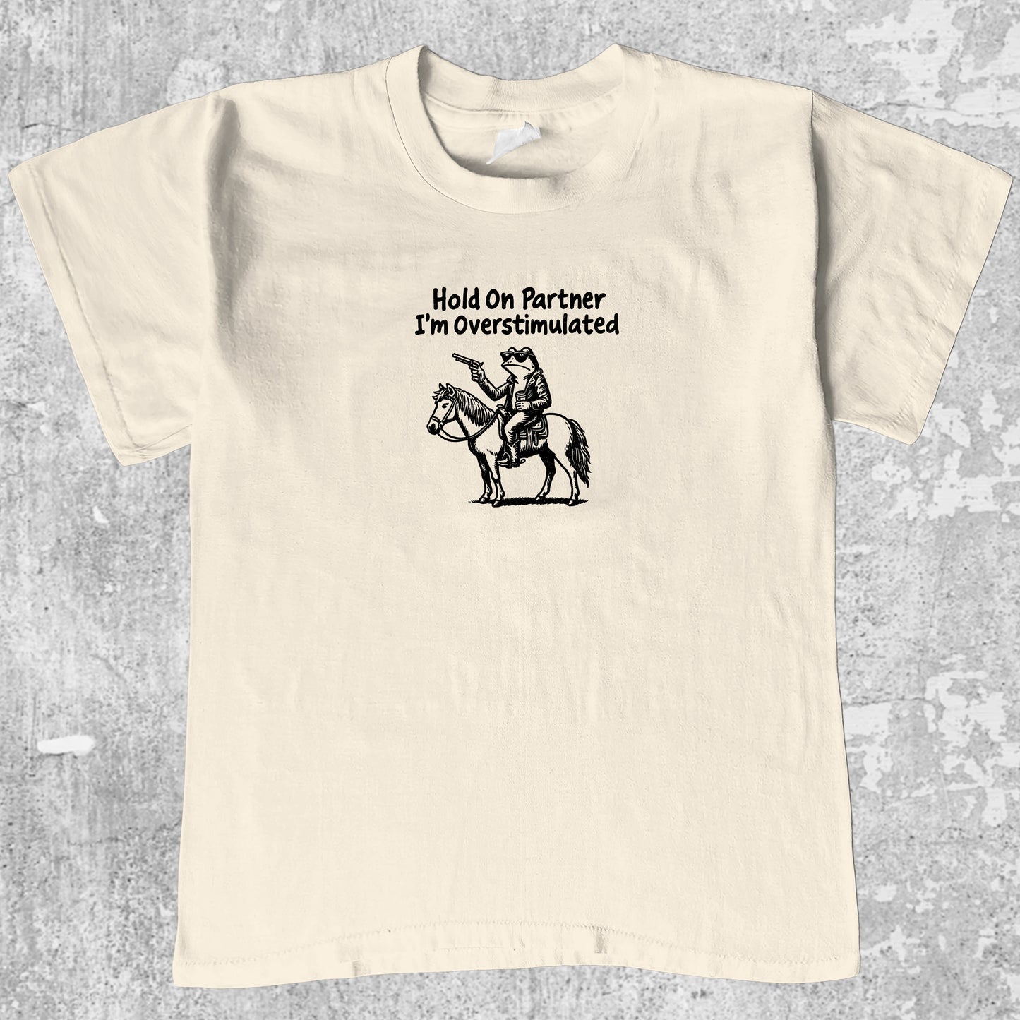 Hold On Partner I'm Overstimulated graphic tee with funny frogs print, retro and trendy graphic. Perfect for Christmas gifts for friends and family. Cream shirt.