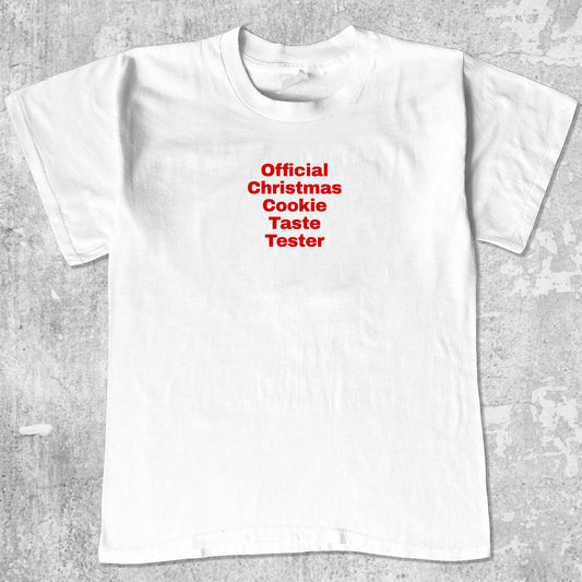 Official Christmas Cookie Taste Tester graphic tee with bold and humorous print, funny and trendy graphic. Perfect for adults and gift-giving. White shirt.